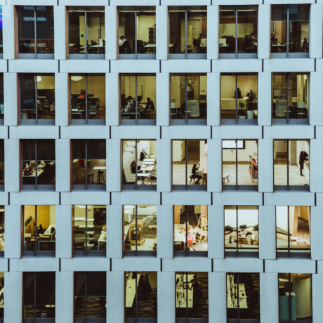 An office building with multiple windows that show various people working inside the building