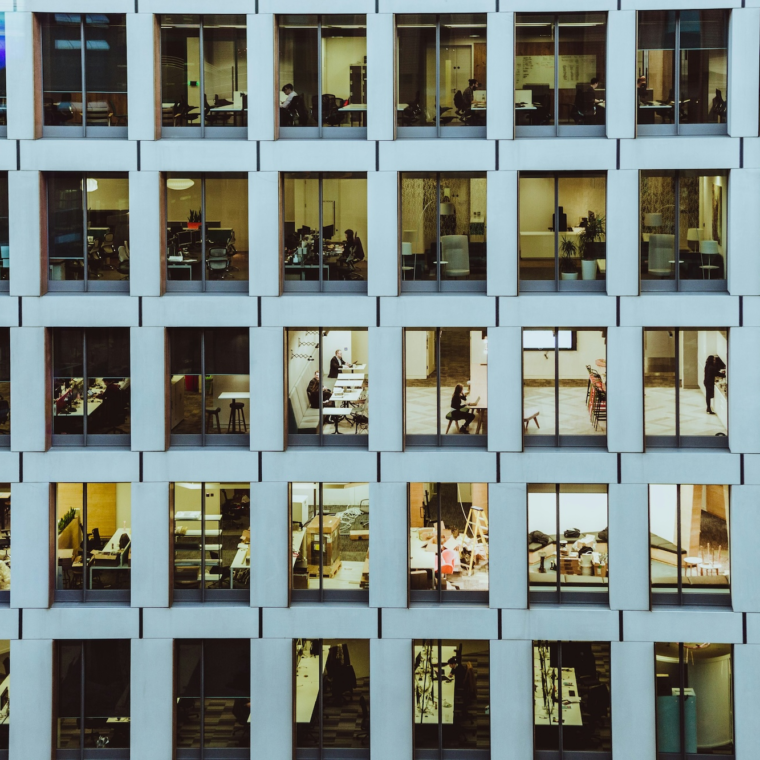 An office building with multiple windows that show various people working inside the building